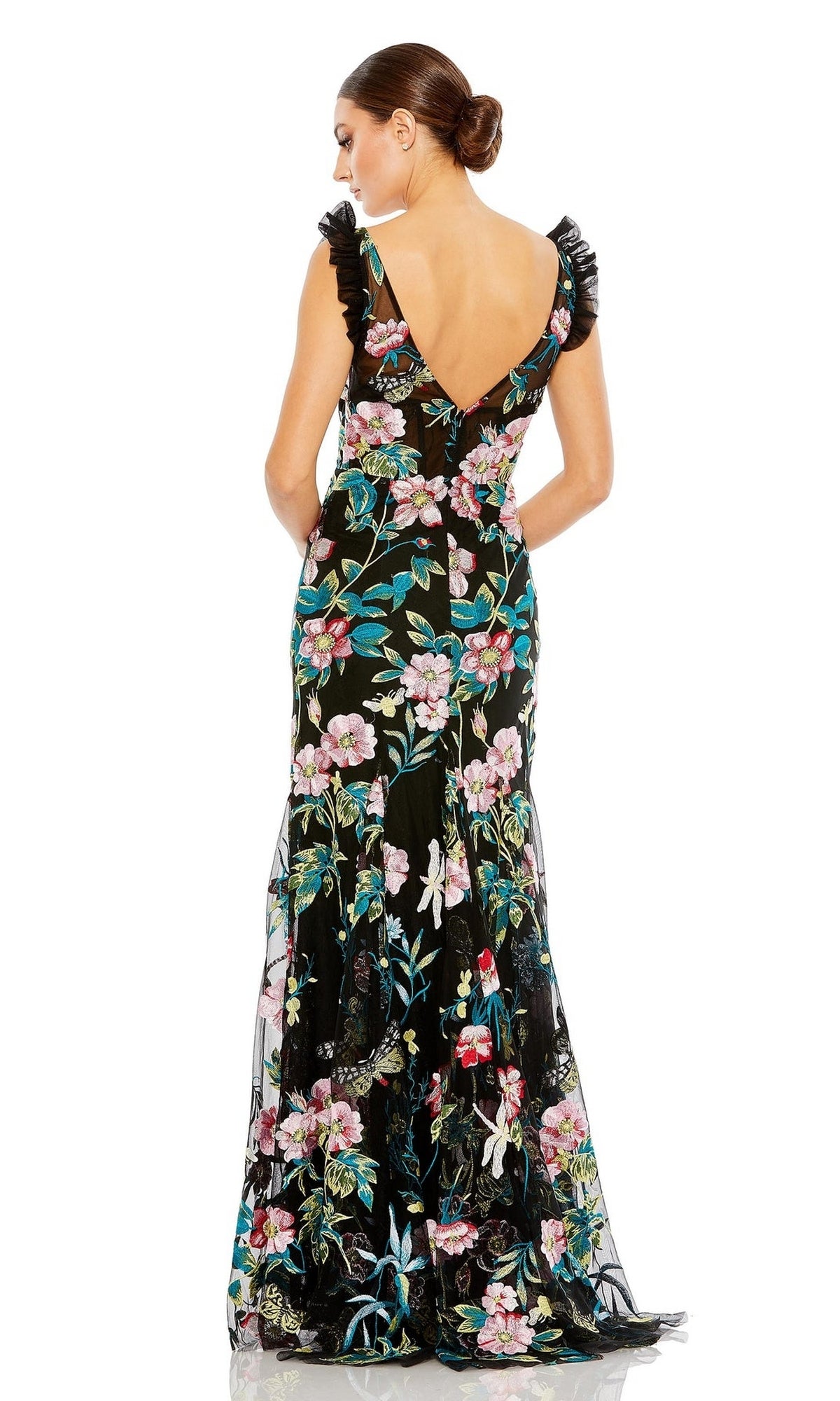 A woman stands facing away, wearing the Mac Duggal Long Formal Dress 68273—an elegant black floral embroidered gown with ruffled shoulder accents, a floor-length skirt, and a plunging v-neckline.